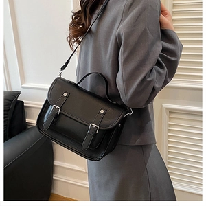 Detail of black crossbody satchel showing premium pebble grain leather and silver buckles