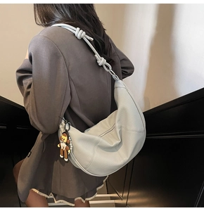Detail of light blue hobo bag with knotted strap and cartoon charm worn by a model