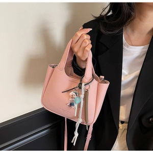 Close-up of pink lychee grain leather bucket bag with cute bear charm and logo detail