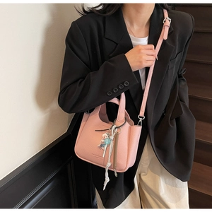 Pink lychee texture bucket bag with adjustable strap and decorative charms worn by a model