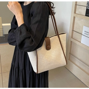 Detail view of woven straw tote bag with brown faux leather trim and round button closure