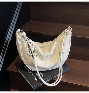 Detail of cream hobo bag with pebble leather texture and decorative knotted shoulder strap