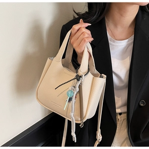 Close-up of off-white lychee pattern leather bucket bag with fashion charm and text detail