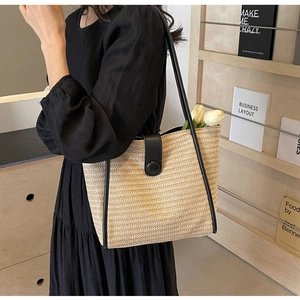 Detail of woven straw tote bag featuring contrast black leather trim and handles