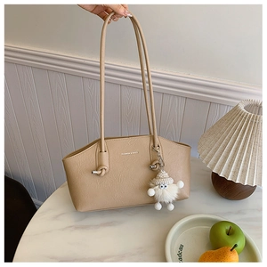 Detail of beige underarm bag with lychee texture, plush charm, and metal logo