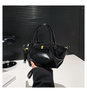 Detail of black glossy leather bucket bag featuring elegant gold metal clasp and strap