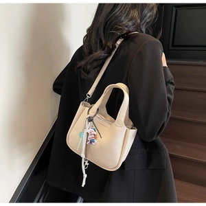 Detail shot of beige lychee leather bucket bag with cute bear charm and shoulder strap