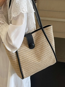 Minimalist woven straw tote bag with black leather trim shown on a model's shoulder