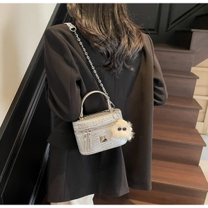 Close-up of a silver woven texture box bag with a metal chain and plush monster charm