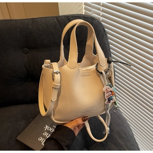 Detail of off-white litchi grain leather bucket bag with cute puppy charm accessory