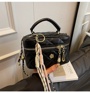 Détail du sac matelassé noir avec ornement fleur dorée et breloque tissée élégante