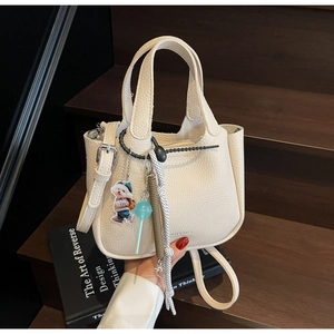 Detail of off-white lychee texture leather bucket bag with cute cartoon charms on wood