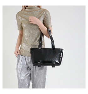 Détail du sac cabas noir brillant avec des œillets métalliques et une finition vernie