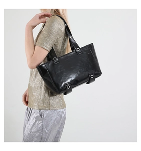 Vue détaillée du sac cabas noir en cuir huilé avec œillets métalliques sur la bandoulière