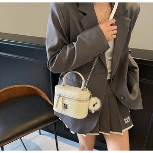 Detail of a creamy white crocodile pattern box bag with plush pendant and chain strap