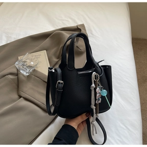 Close-up of black lychee leather handbag featuring cute bear charms and a woven rope strap