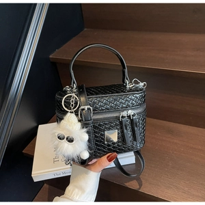 Detail of black woven texture box bag featuring dual zippers and plush ball charm