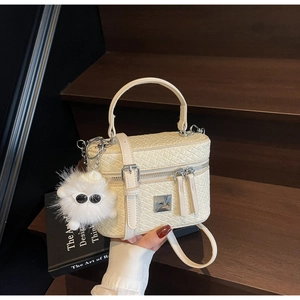 Detail of cream woven box bag with metal plate and fluffy monster keychain on wood stairs