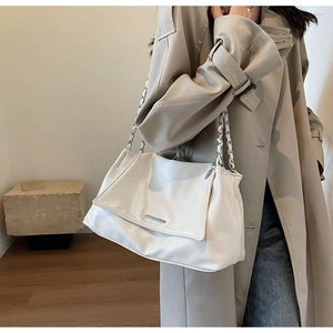 Détail du sac fourre-tout en similicuir blanc cassé avec chaîne argentée sur trench beige