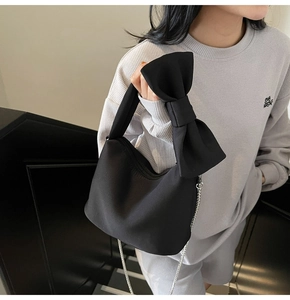 Detailed view of black fabric handbag featuring a large bow and silver metal chain strap