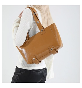 Détail du sac cabas en cuir marron avec œillets argentés porté par un mannequin mode