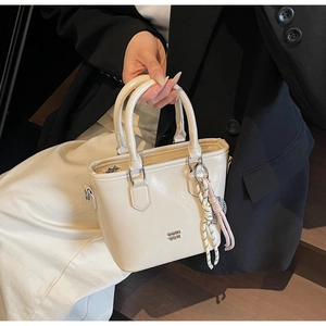Détail du sac seau beige en cuir ciré avec logo métallique et pendentif tressé