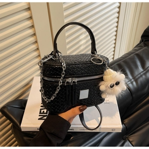 Close-up of black woven texture box bag featuring metal chain and plush monster charm