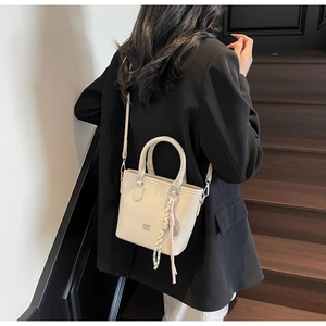 Détail du sac seau en cuir crème avec pendentif tressé et logo de haute qualité