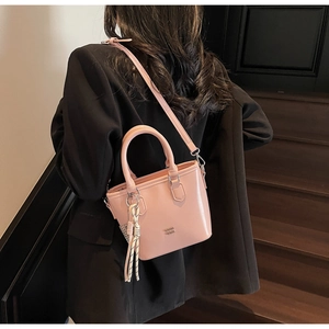 Détail du sac seau rose en cuir ciré avec poignée et pompon sur l'escalier