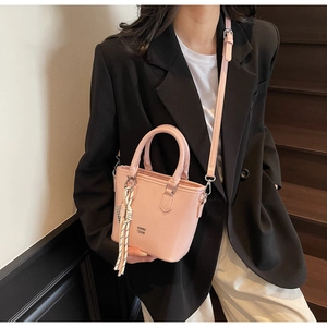 Sac seau en cuir ciré rose avec glands présenté sur des escaliers en bois avec modèle