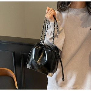 Detail of glossy black leather bucket bag with silver metal corners and chain strap
