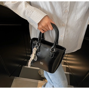 Détail d'un sac seau en cuir verni noir avec foulard en soie et logo métallique de marque