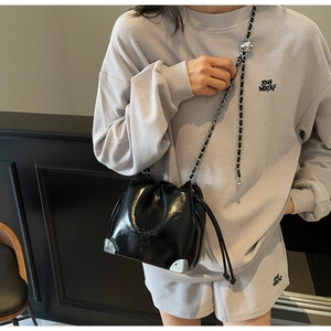 Detail of black glossy drawstring bucket bag with silver metal corners and chain strap