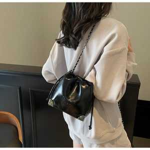 Detail of black glossy leather bucket bag with silver chain strap and metal corners