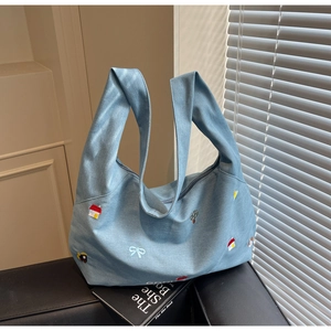 Dettaglio della borsa tote in denim azzurro con ricami colorati di case e alberi
