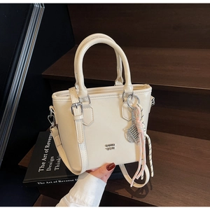 Détail d'un sac seau crème avec logo métallique et breloque tressée sur escalier en bois