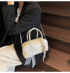 Detail of cream pillow bag with lace bow and colorful tassel charms on a black blazer