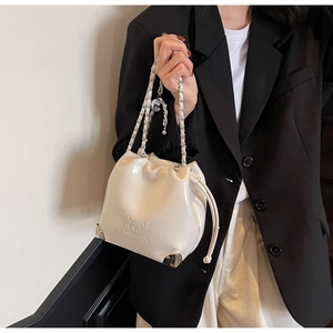 Detail of cream leather bucket bag with drawstring closure and metal corner protectors