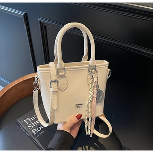 Détail d'un sac seau crème avec pendentif de raquette de tennis sur une chaise noire chic