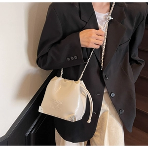 Detail of cream bucket bag with embossed logo lettering and silver metal corners