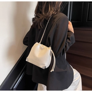 Detail of cream drawstring bucket bag with embossed logo and silver corner protectors