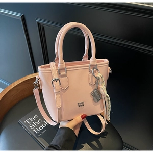 Détail d'un sac seau rose pâle avec logo en métal, pompon coloré et bandoulière réglable