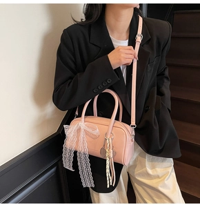 Pink pillow handbag with white lace bow detail and braided pendant worn by a model