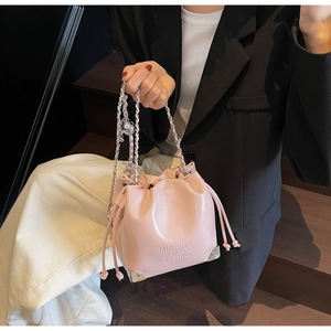 Pink drawstring bucket bag with silver metal corners and brand logo detail on wood stairs