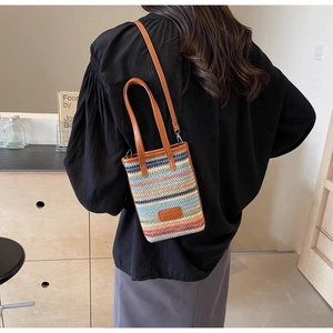 Close-up of rainbow striped straw woven bag with brown leather handles and shoulder strap