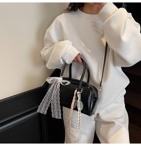 Detail showing the black Boston bag with lace bow and metal tennis racket charm on shoulder