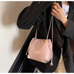 Pink glossy leather bucket bag detail with metal corners and chain strap worn by a model