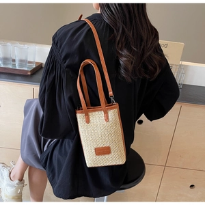 Detail of a woven straw crossbody bag with brown leather trim and handle on a model
