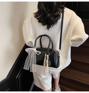 Detail of black Boston bag with white lace bow and tennis racket charm accessory
