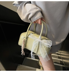 Detail view of a mint green Boston bag with white lace bow and pink woven tassel charm